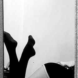MandyX, an OnlyFans model, showcases her unique style in a mirror selfie. In this image, she is seen wearing black stockings and heels paired with a white top. The background is simple and uncluttered, allowing her to be the focal point of the image.