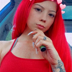 Red-haired Amber in a red tank top, posing with a hand on her chin and finger nail polish