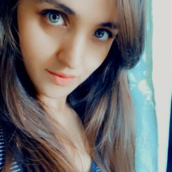 A young woman with long hair in a blue shirt, smiling and posing for the camera.