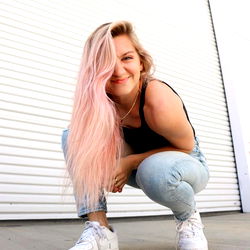 Anna, a young adult female with pink hair, crouched in a white sneaker and smiling at the camera