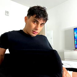 Riley, a young and charming man, is captured in an intimate moment on his OnlyFans VIP page. In the image, he is lounging on a bed, clad in casual attire, and radiates an air of relaxed confidence.