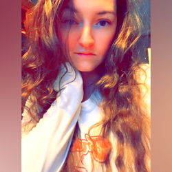 Aura Nova, a young adult woman with wavy hair and glasses, posing for an OnlyFans promotional photo.