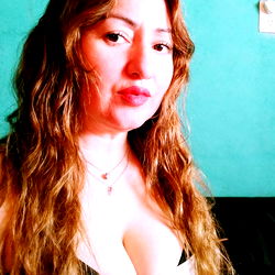 Adelcy❤️, a model with long wavy hair and a sleeveless white top. She is posing for a photo with a blue background.