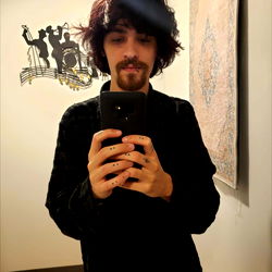 An individual with long hair and tattoos, holding a phone in front of them.