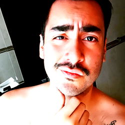 Young Man in a Shirtless Selfie with Mustache and Tattoo