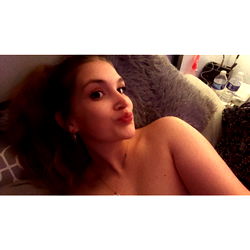 A Shirtless Selfie of a Young Woman Posing for the Camera on a Bed