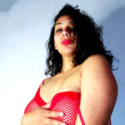 Soffi 🦋🖤, a vibrant and lively OnlyFans model posing confidently in a red mesh garment against a white wall. She's radiating energy and allure.