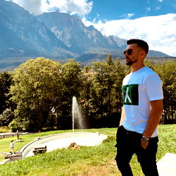 A man posing in front of a scenic mountain landscape with the word 'KING' on his shirt.