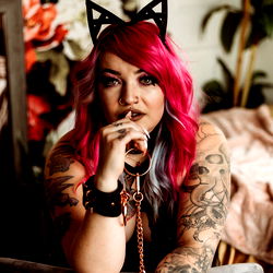 Raven Mae, Tattooed Model in Stylish Outfit and Cat Ears, Sitting and Smirking