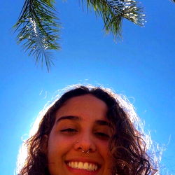 Ana, 25, smiling outdoors at the beach