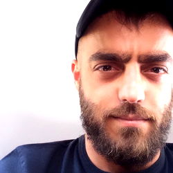 A man with a beard and mustache, partially visible on the right side of his face, looking to the side.