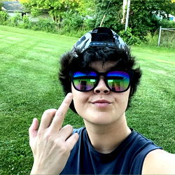 Kenzie, a young adult in sunglasses, makes a playful gesture with her hand in front of her face.