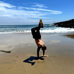 Strongly built fitness model performing yoga on beach