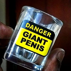 A humorous image of a shot glass with a cautionary label, placed in front of a person.