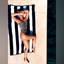 Onlyfans Model Adeline D. lounging on beach towel with striped pattern.