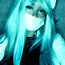 Ana surfi, a model with striking blue hair and matching cat ears, poses in a unique costume. The background features an industrial-looking setting.