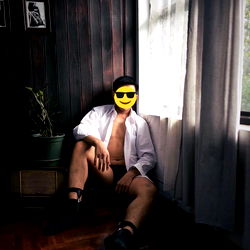 Sweetman69 in an Asian Home, Seated Casually with Window and Plants in the Background.