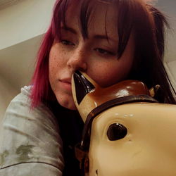 Amanda, a young woman with pink hair, expressing affection towards a plush toy by playfully nibbling its ear