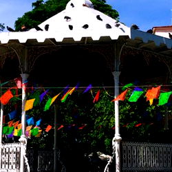 Colorful Flags on Poles at a Distance, with a Building and Trees in the Background