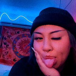 A young woman playfully pointing at the camera in a selfie with a colorful backdrop.