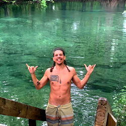A man with a surfboard, celebrating in a river near the forest. 🌿