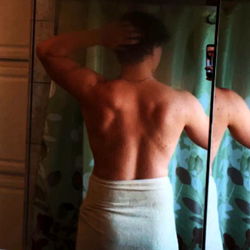 Full-length mirror reflection in the bathroom of a shirtless man