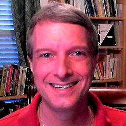 A man in a living room with bookshelves in the background, smiling at the camera.