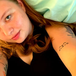 Hazel Marie in a black dress, capturing a selfie with her tattoos and piercings on full display. Onlyfans model from the USA,