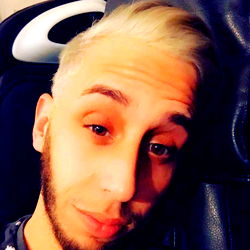 A young man with a beard, sporting a blonde hairstyle and wearing a black tank top.