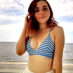 ArticJune, a captivating OnlyFans model posing in a blue and white bikini by the ocean.