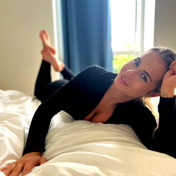 Alice Elena, a stunning model in her prime, lying comfortably on the bed with her head propped up on one hand.