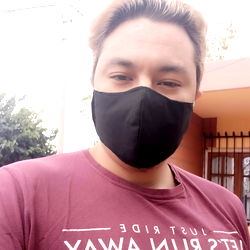 A person in a mask taking a selfie with their back to the camera, standing outdoors against an overcast sky.