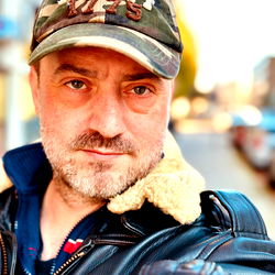 Casually Dressed Man in Camouflage Cap and Leather Jacket Taking Selfie Outdoors