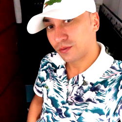 Stylish Mr Abadia posing for the camera in a colorful shirt and white cap with green logo, set against a blurred background. He's based in Rio de Janeiro.