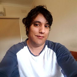 Adrian, a young adult with short hair, taking a selfie in their room.