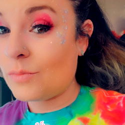 Auburn-haired girl in colorful tie-dye shirt with pinkish makeup and rainbow unicorn vibes