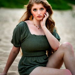 Astrid, a Louisiana-based model, sitting on a sandy beach with her hand to her chin and looking off into the distance.