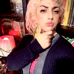 An individual posing in front of a bookshelf with a book