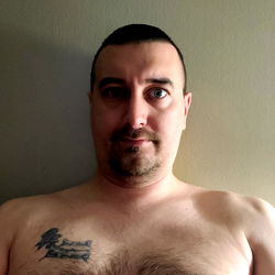 A shirtless man with a tattoo, sitting in front of a mirror.