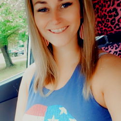 Caitlin, a Texas-based OnlyFans model in a blue jean tank top with American flag sleeves posing for the camera.