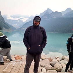Adventurer at a scenic lake with mountains in the background, standing on a dock