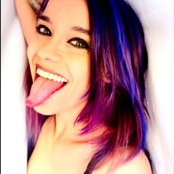 Model in colorful hair and blue outfit with tongue out