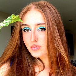 Anaïs, a young female with vibrant makeup and an exotic green leaf accessory in her hair.