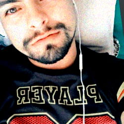 Andru Herrera, a young man from Colombia, relaxing in a black shirt with headphones around his neck. He is lying down and looking directly at the camera, giving off a laid-back vibe. His unique style and cool demeanor make him stand out!