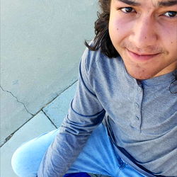 A young man with long hair sitting on a blue bag