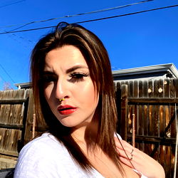 Fashion-forward Ari in a casual white top, striking a pose outdoors on a sunny day.