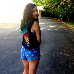 Ayla, a young woman in blue jean shorts and a black tank top with a unique back design, standing confidently on the asphalt. She's looking directly at the camera.