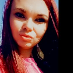 A.ReNeE, a young woman with vibrant red hair, stands confidently in a pink shirt. Her eyes are directed towards the camera as she poses for this portrait.