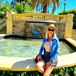 Woman posing for photo at a fountain with a city background.