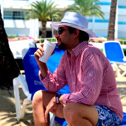Man in Hat Sipping Drink at Beach